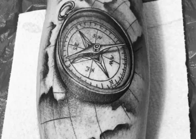 Schwarz-weißes Bein Tattoo - Kompass liegend auf einer Karte
